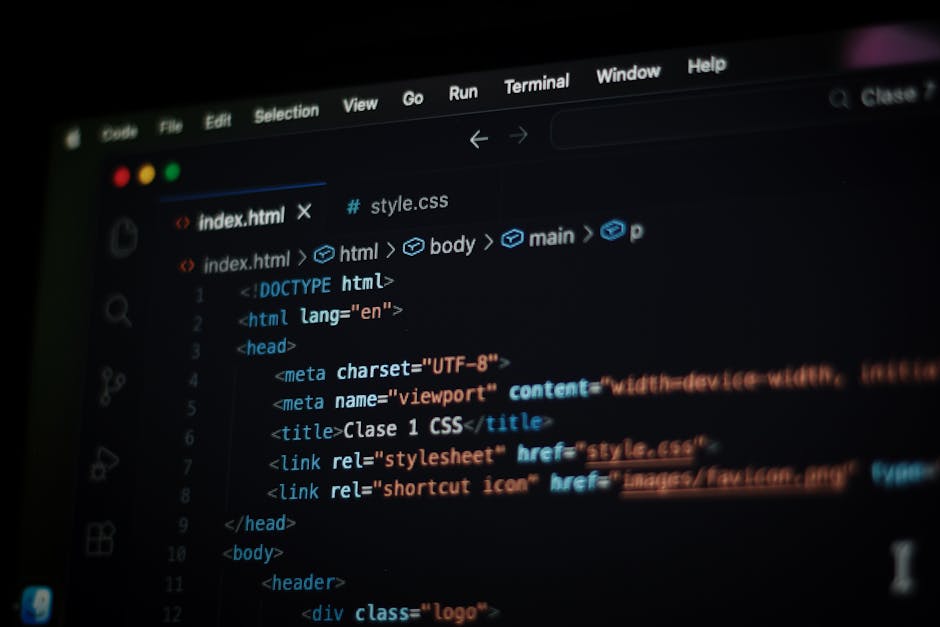 A close-up view of a person's hand resting on the keyboard of a modern silver laptop placed on a wooden desk. The laptop screen displays lines of programming code in a text editor with syntax highligh